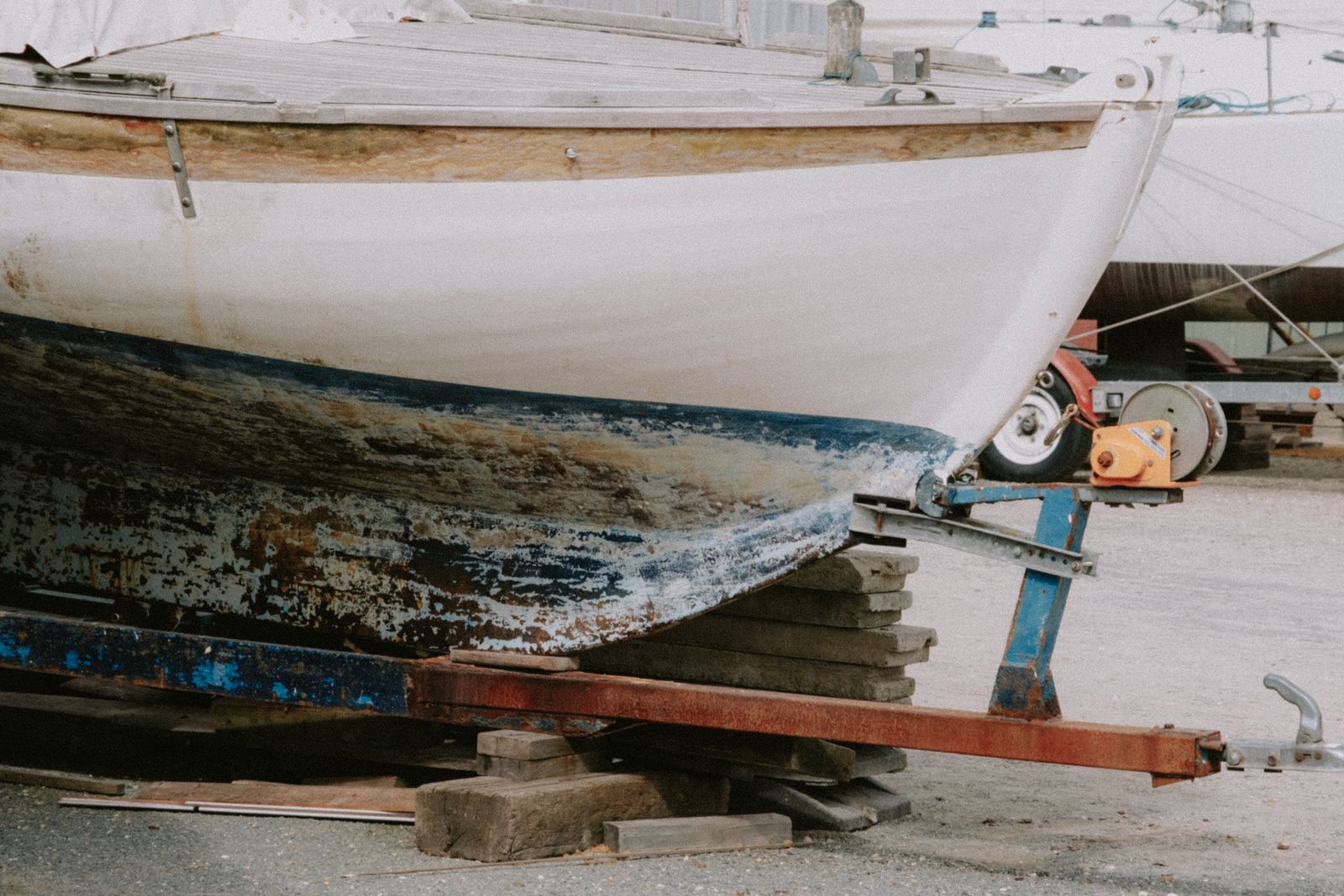 Sailboat hull on stands in a boatyard with worn, damaged bottom paint