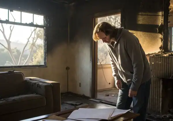 Man in a fire-damaged home reviewing paperwork for a denied fire claim.